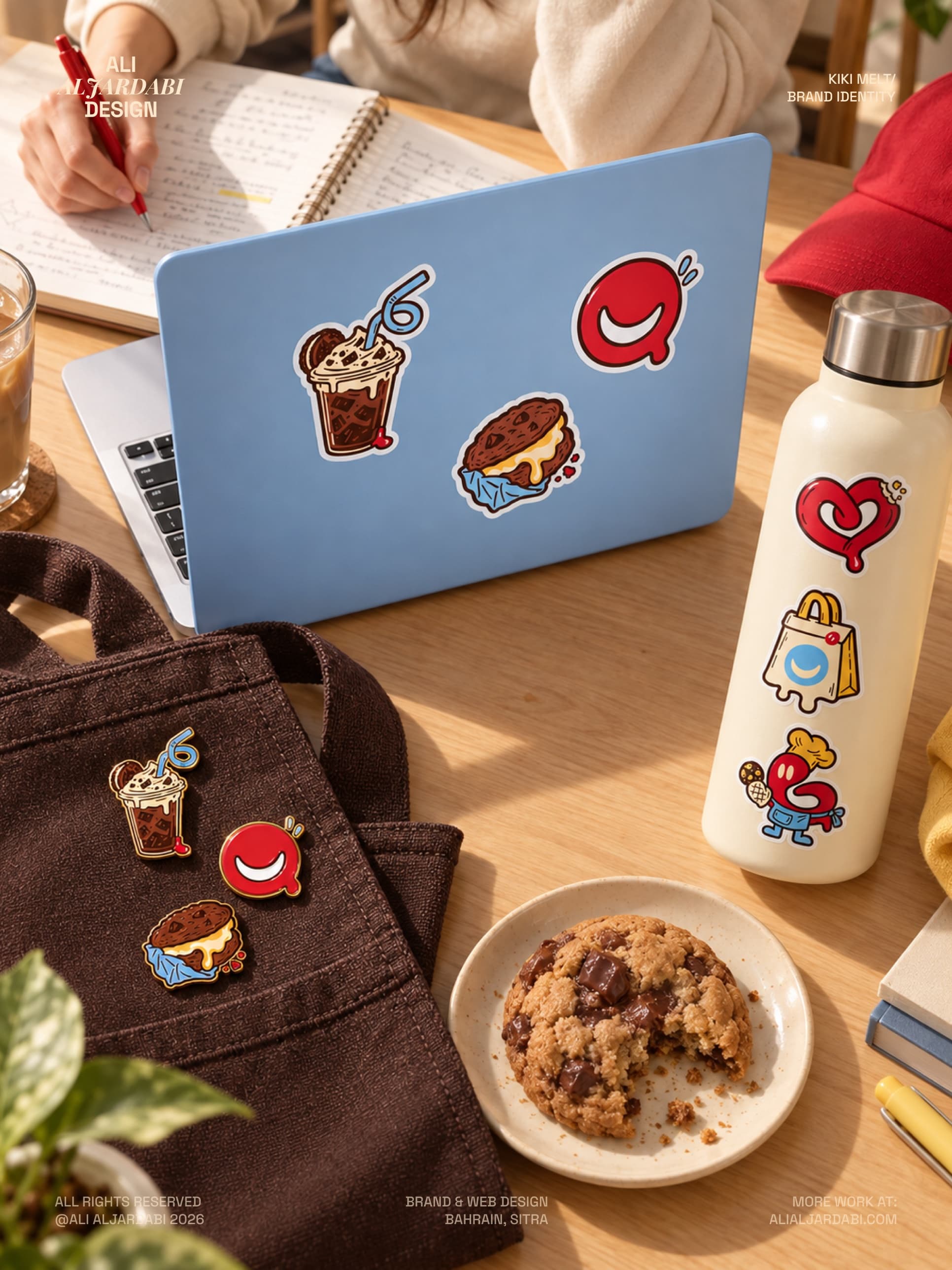 Kiko Melt stickers on a blue laptop lid and a cream bottle, with matching enamel pins on a brown tote, beside a chocolate chip cookie on a plate